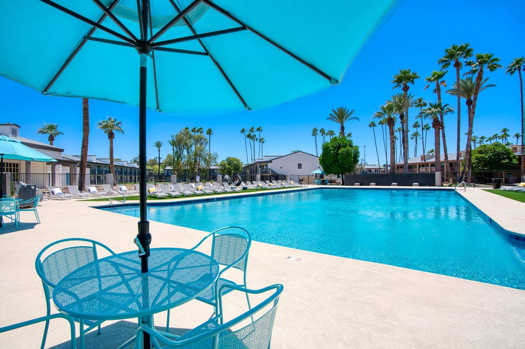 a swimming pool with tables and chairs under an umbrella at Presidio Palms Apartments, Arizona