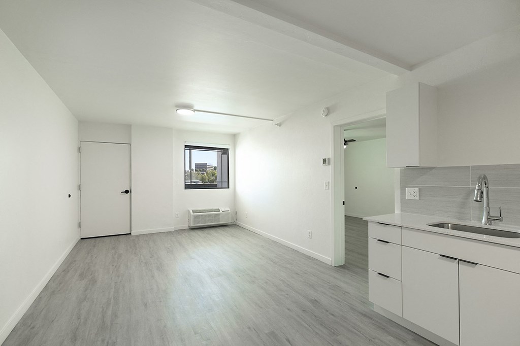 A spacious room with a window, a door, and a kitchen area with a sink and white cabinetsat Presidio Palms Apartments, Tucson, Arizona