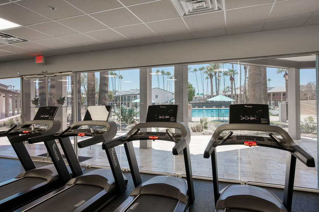 a gym with cardio machines and a view of a swimming pool at Presidio Palms Apartments, Tucson