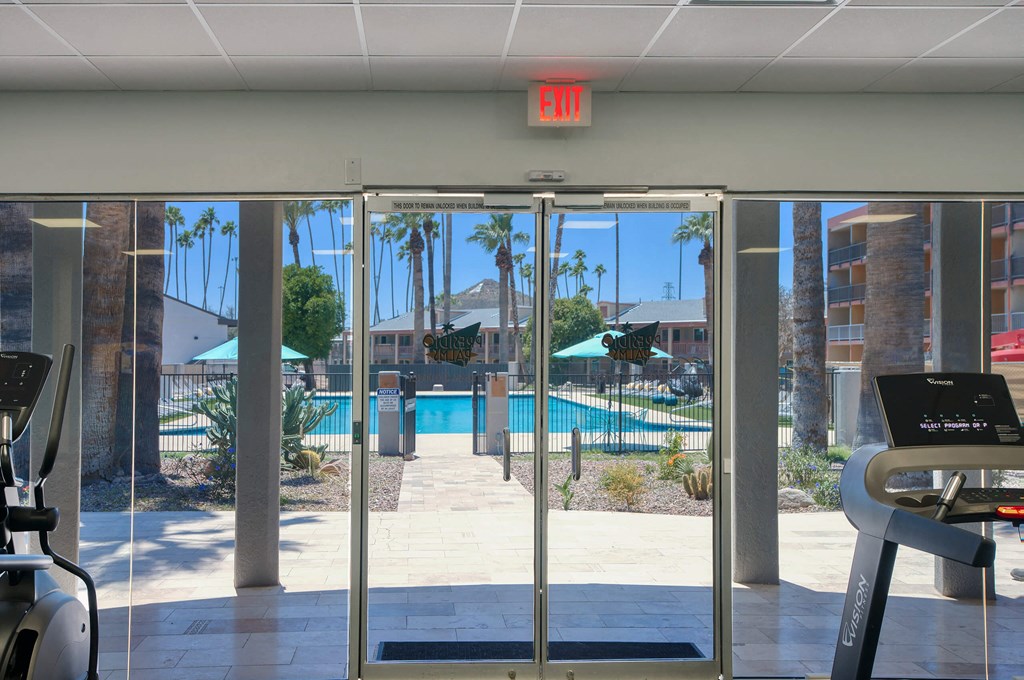 a view of a swimming pool from a gym with glass doors at Presidio Palms Apartments, Tucson, AZ