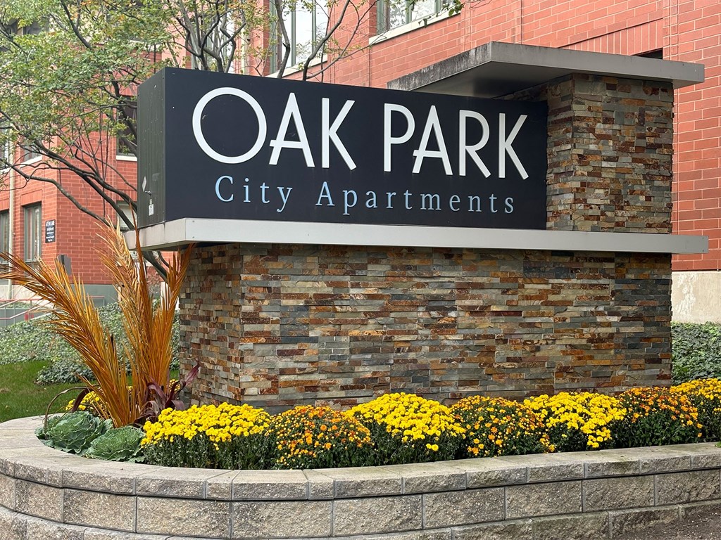 A sign for Oak Park City Apartments is displayed in front of a brick building.