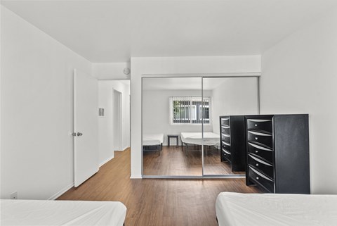 A bedroom with mirrored closet doors, dressers, and beds