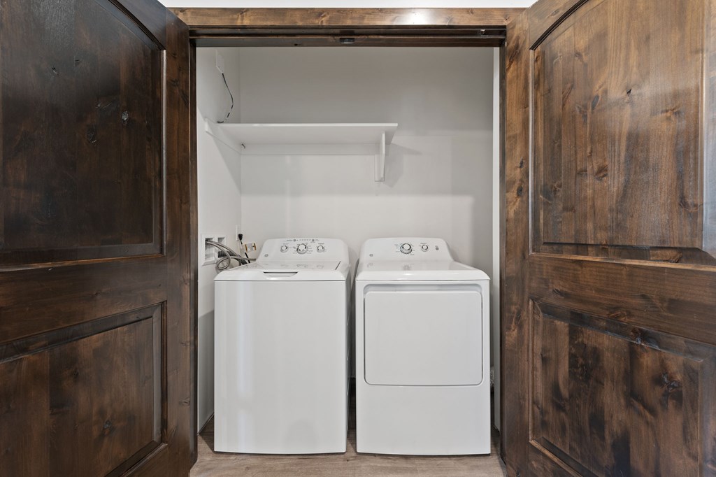 Two white washing machines in a wooden cabinet.