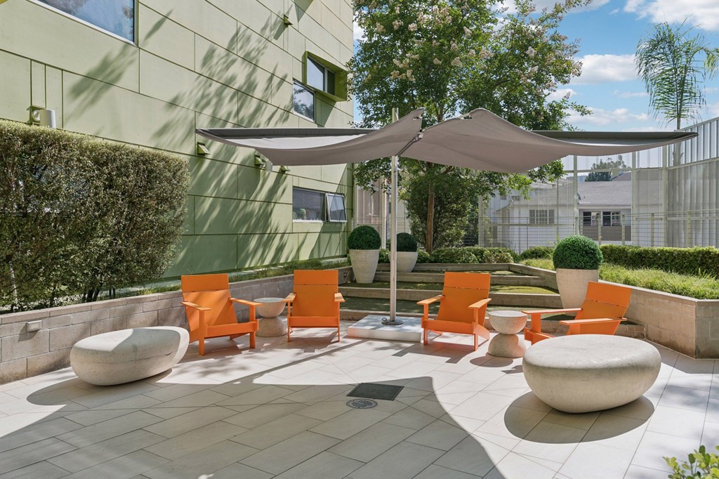 A patio with orange chairs and a white umbrella.