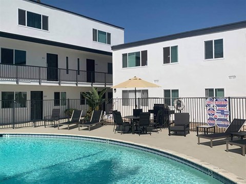 a resort style pool with chairs and umbrellas in front of two buildings