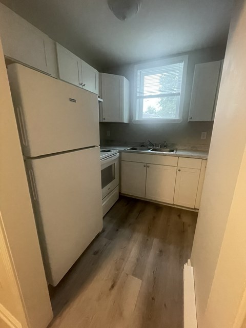 A white refrigerator is in a kitchen with wooden floors.