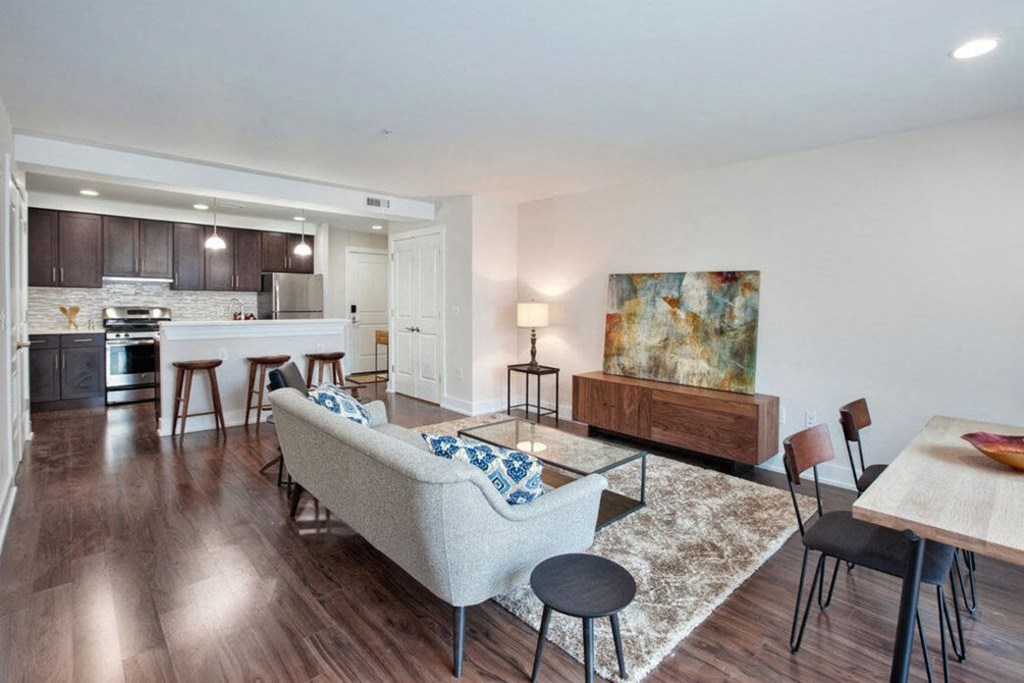 a living room with a couch table and chairs and a kitchen in the background
