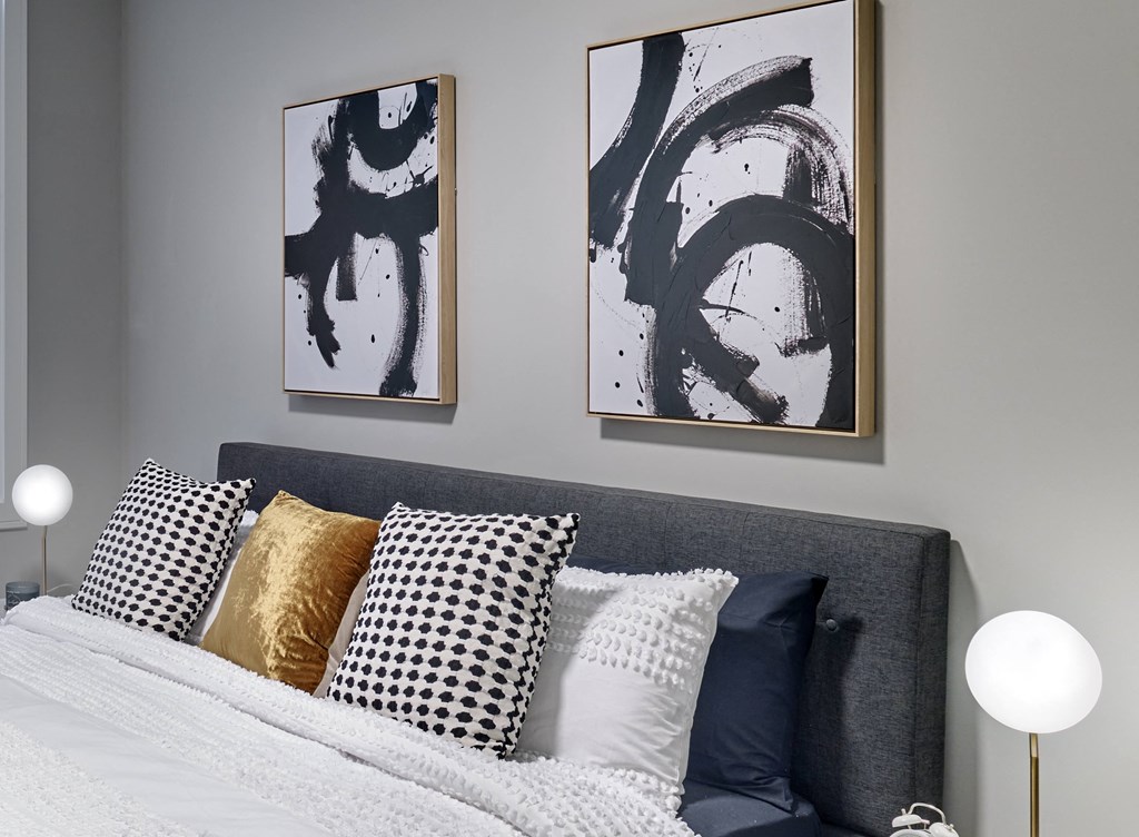 A bed with a grey headboard and pillows in front of two framed artworks.