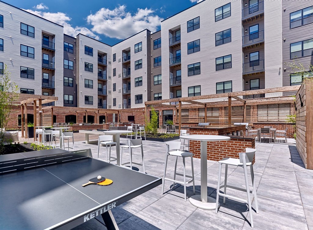 A Kettler table tennis table is in the foreground of a courtyard with apartment buildings in the background.