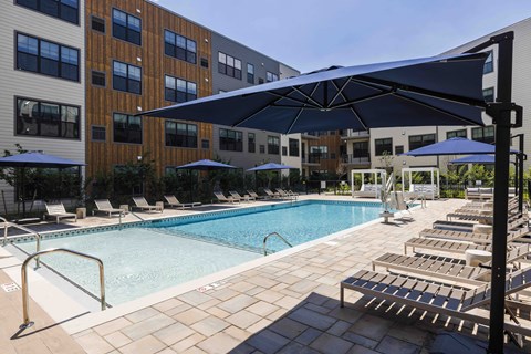 A large outdoor swimming pool surrounded by sun loungers and umbrellas.