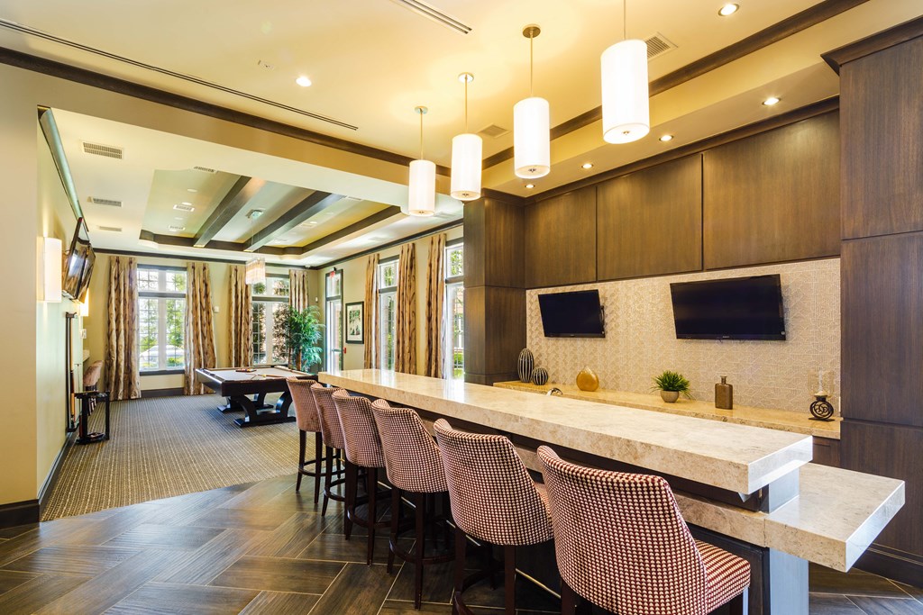 A long marble table with red chairs is in a room with a long window.