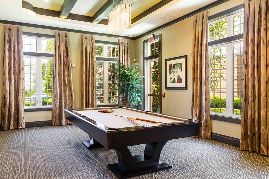 A pool table in a room with large windows and curtains.