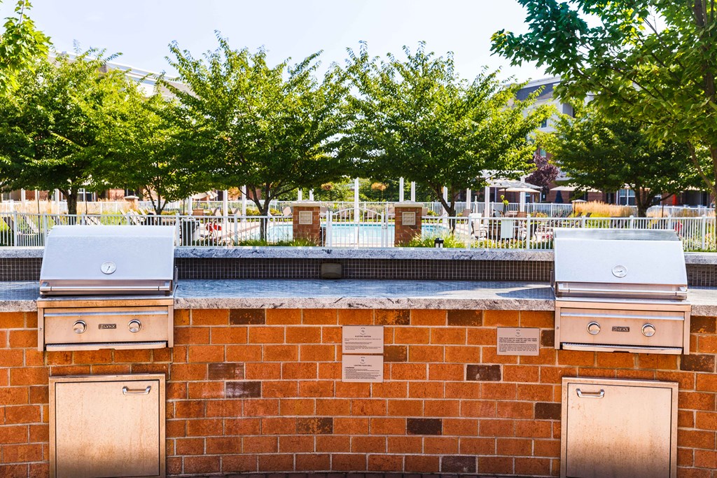 Two grills on top of a brick wall with trees in the background.