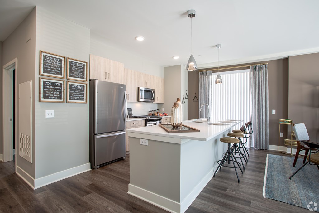 A kitchen with a refrigerator, bar stools, and a dining area.