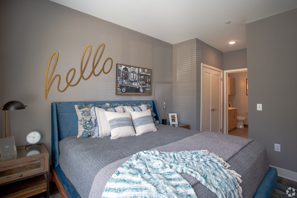 A bedroom with a bed, a nightstand, and a wall decoration with the word "hello" written on it.