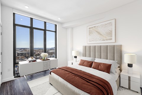 Bedroom with upholstered headboard and large windows at Bay One Apartments, Bayonne
