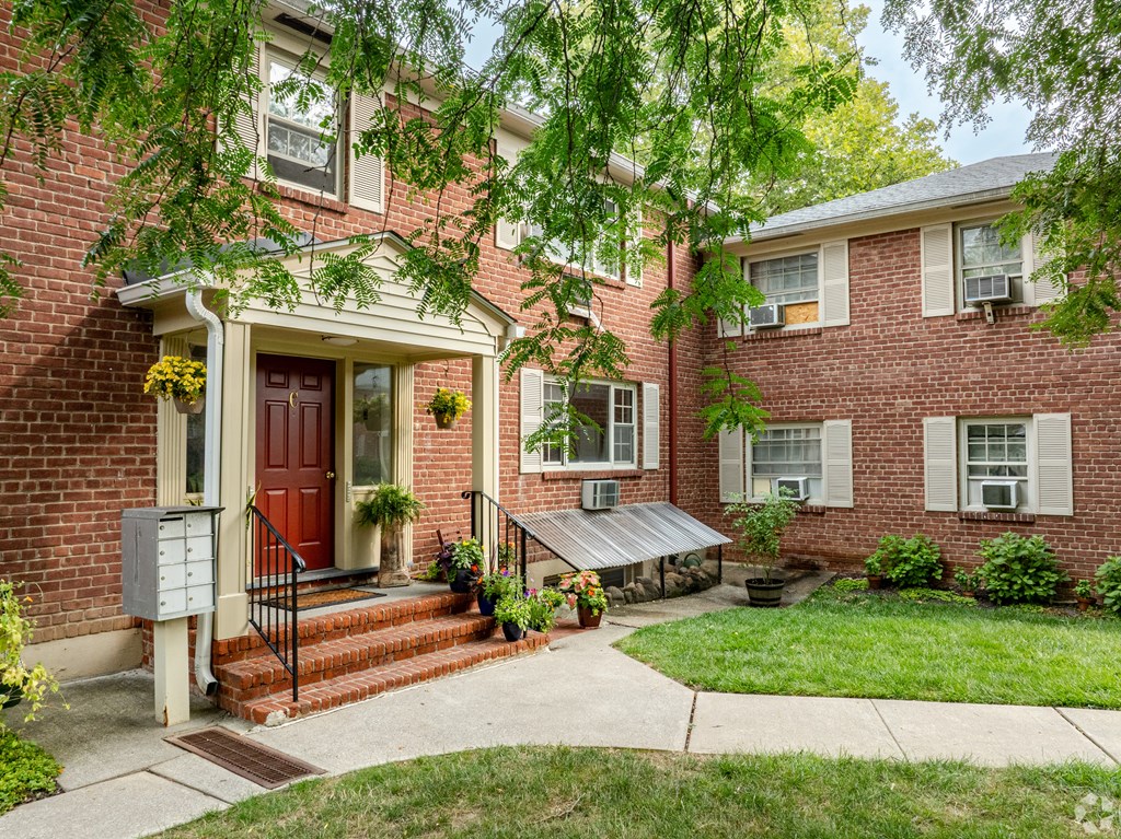 A red door is on the left side of a brick house.