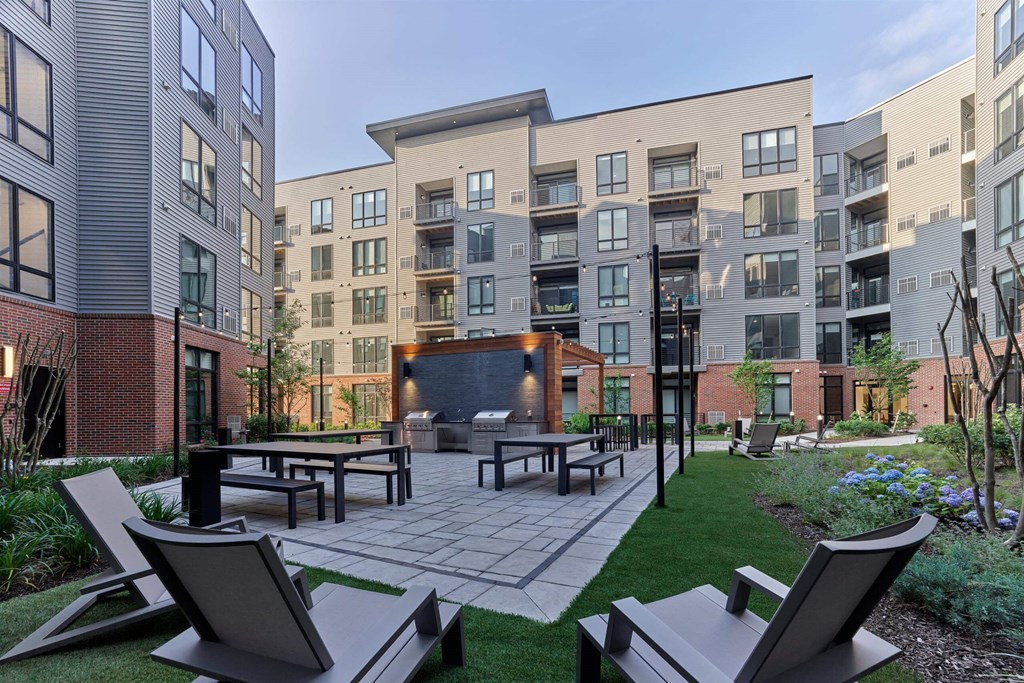 A patio with chairs and a fire pit in front of apartment buildings.