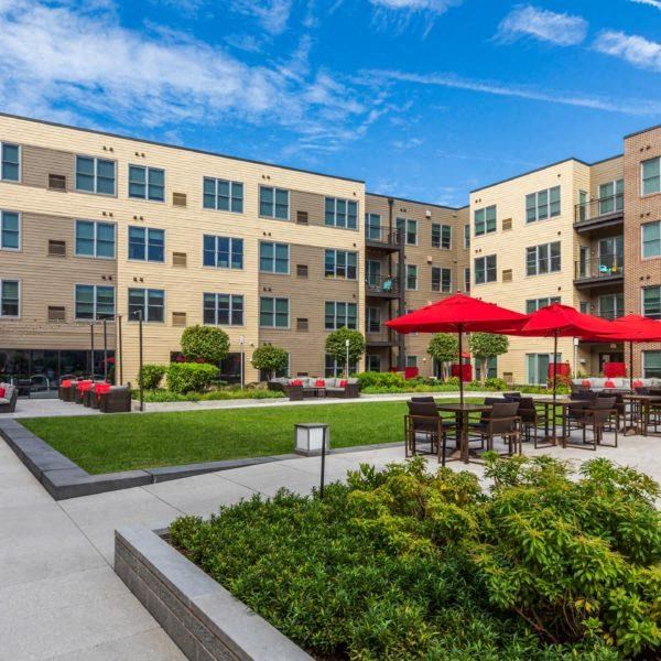 a courtyard with tables and umbrellas in front of an apartment building
