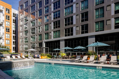 A swimming pool with chairs and umbrellas in front of a building.