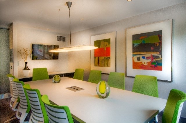 a dining room table with green chairs and paintings on the wall