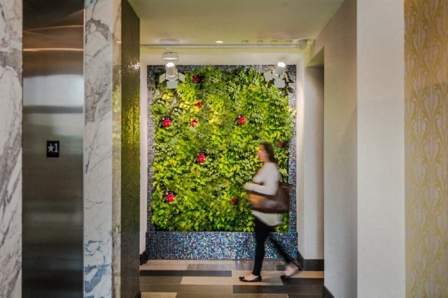 a woman walking in front of a green wall with flowers