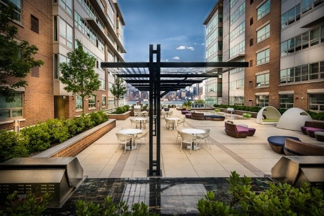 A modern outdoor seating area with tables and chairs is surrounded by brick buildings.