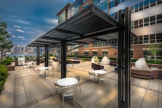 A rooftop patio with white chairs and tables under a black metal awning.