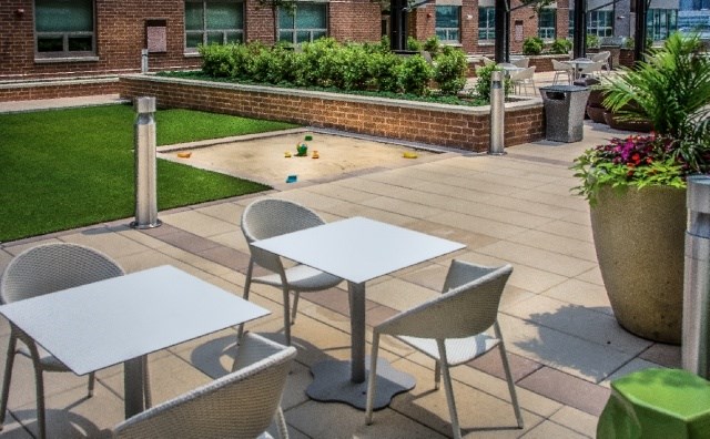 A patio with a table and chairs is surrounded by a brick wall and a green trash can.