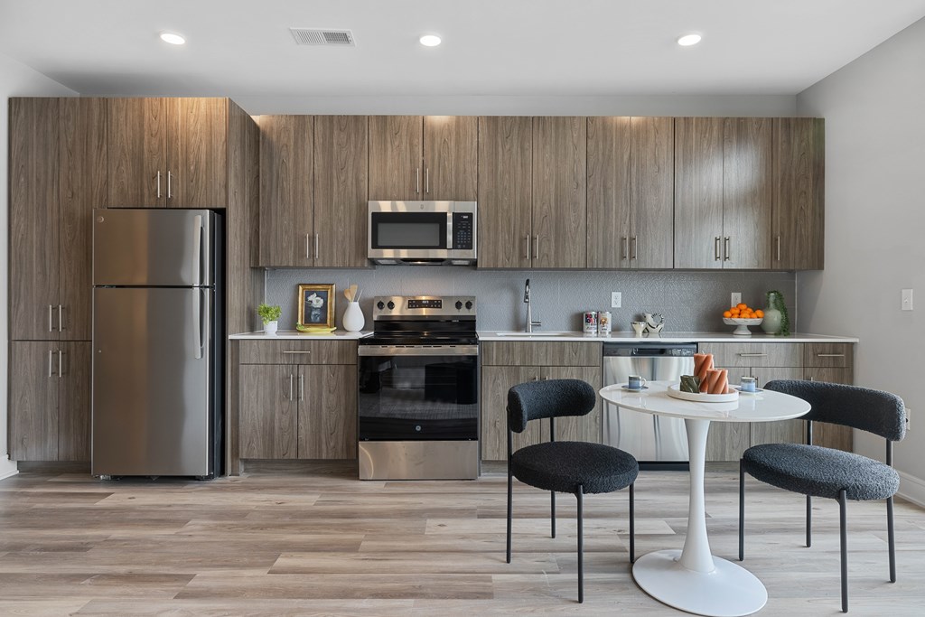 A modern kitchen with a refrigerator, oven, microwave, and a dining table with chairs.