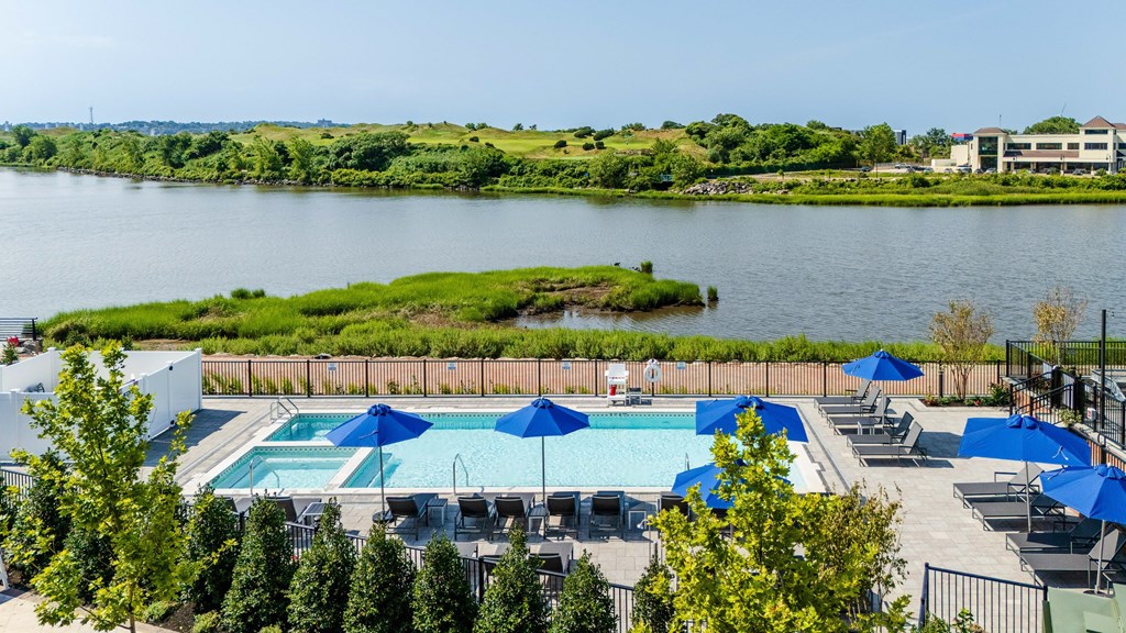 A pool area with blue umbrellas and a view of a river.