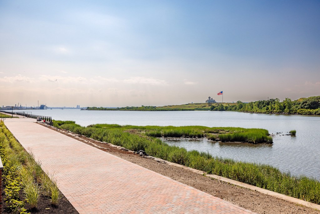 A walkway with a brick pattern leads to a body of water with a flag flying in the distance.