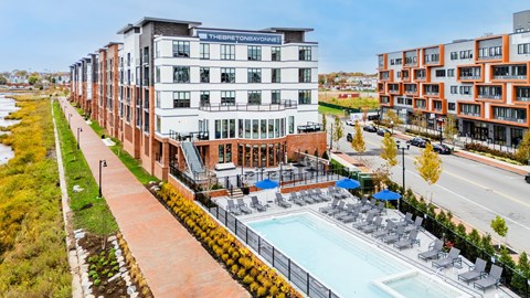 A pool area with lounge chairs and umbrellas is surrounded by a brick walkway and greenery.
