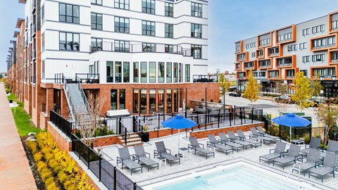A pool area with lounge chairs and umbrellas in front of a multi-story building.