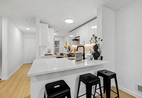 A kitchen with white countertops and black stools.