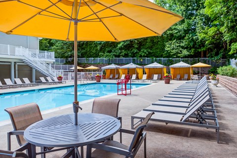 A large yellow umbrella is in the foreground of a pool area with sun loungers and tables.