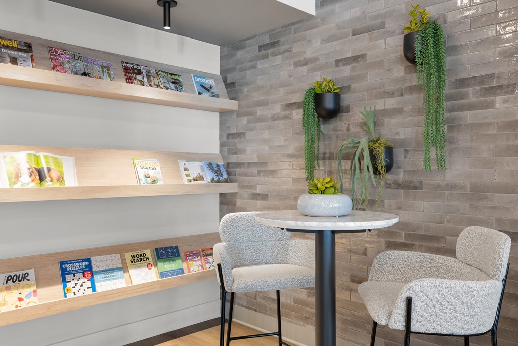A room with a table, two chairs, and a wall with books and plants.