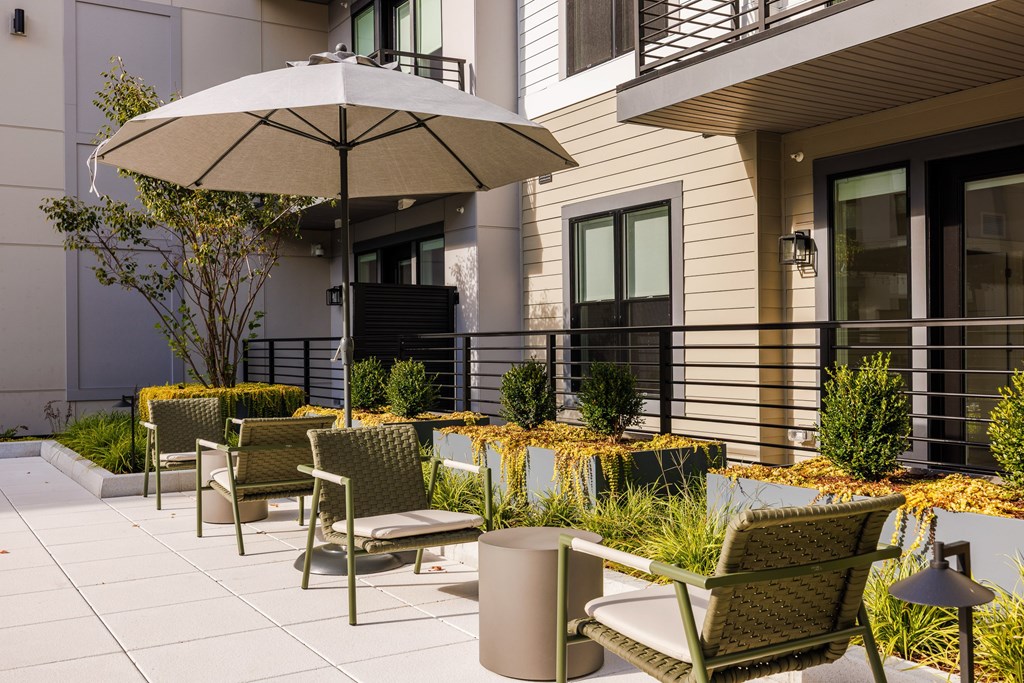 A patio with a white umbrella, chairs and a table.
