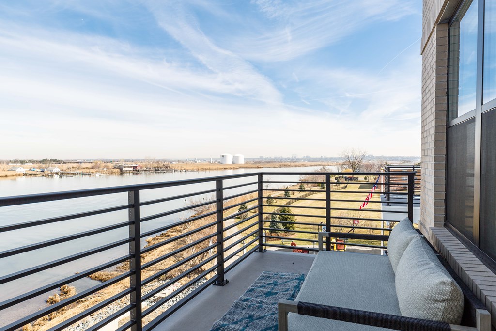 A balcony with a metal railing and a grey cushioned bench overlooks a body of water.
