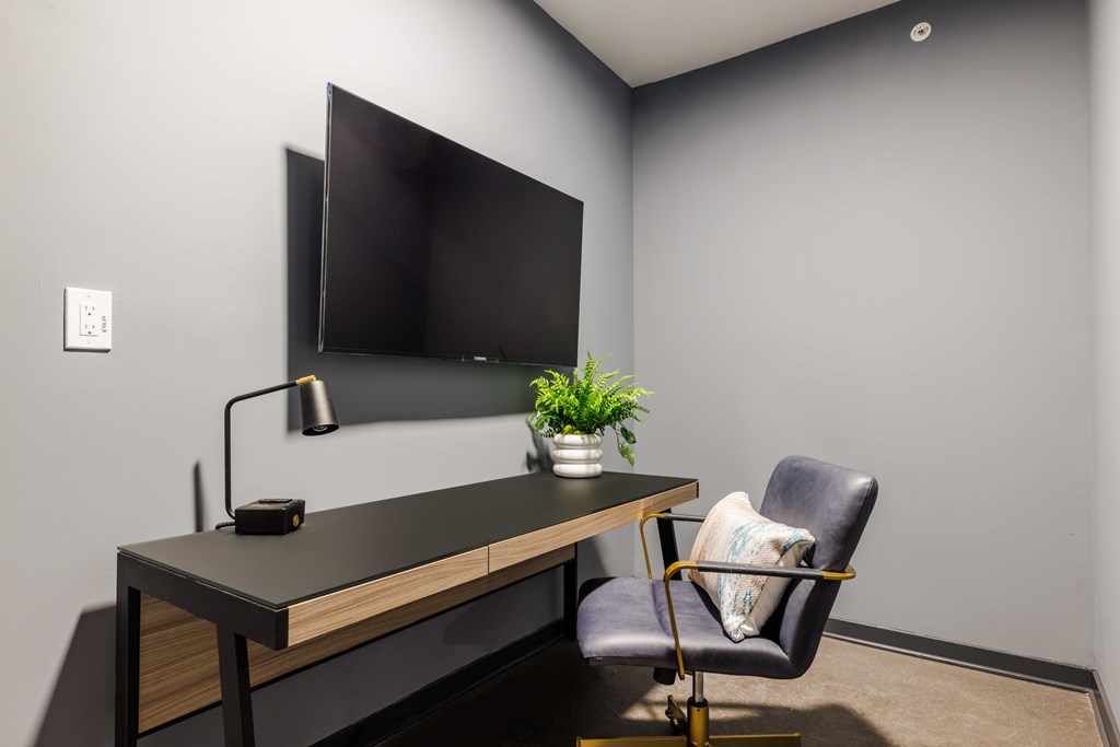 A black desk with a plant and a chair in front of a grey wall.