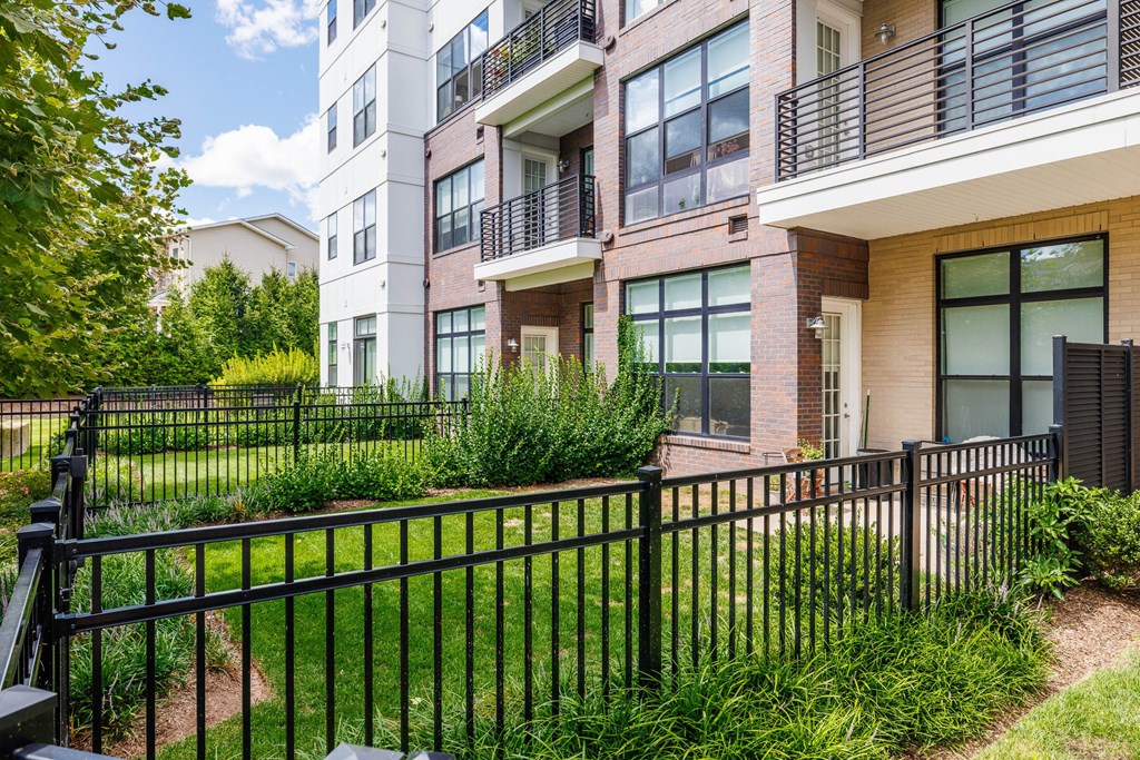 A black metal fence surrounds a grassy area in front of a multi-story apartment building.