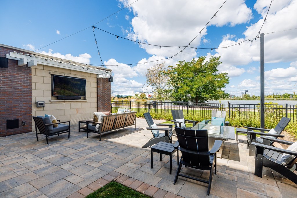 A patio with black chairs and a television on a brick wall.