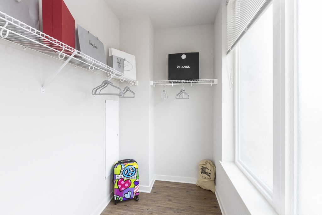 a room with a window and a closet with shelves and a suitcase