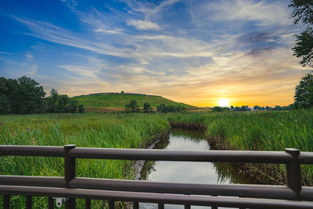 A sunset view over a grassy field with a wooden fence in the foreground.
