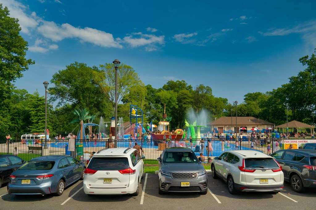 A parking lot with several cars and a playground in the background.