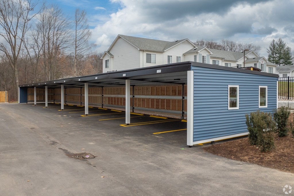 A blue building with a black roof is in the foreground with a parking lot in front of it.