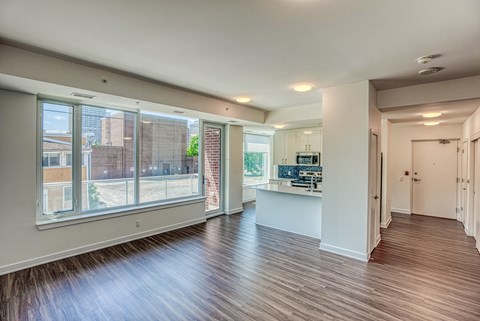 an empty living room with a large window and a kitchen