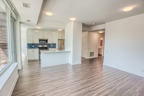 an empty living room and kitchen with white cabinets and wood flooring