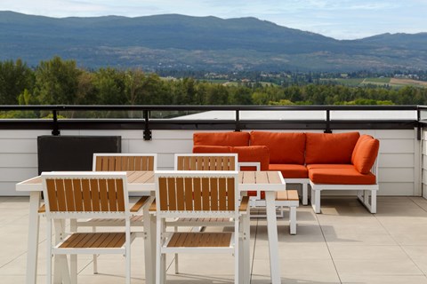 A white table and chairs with orange couches on a balcony overlooking a valley.