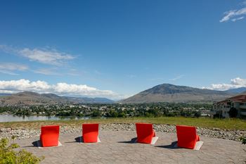 Three red chairs are placed on a stone patio overlooking a town and a mountain.